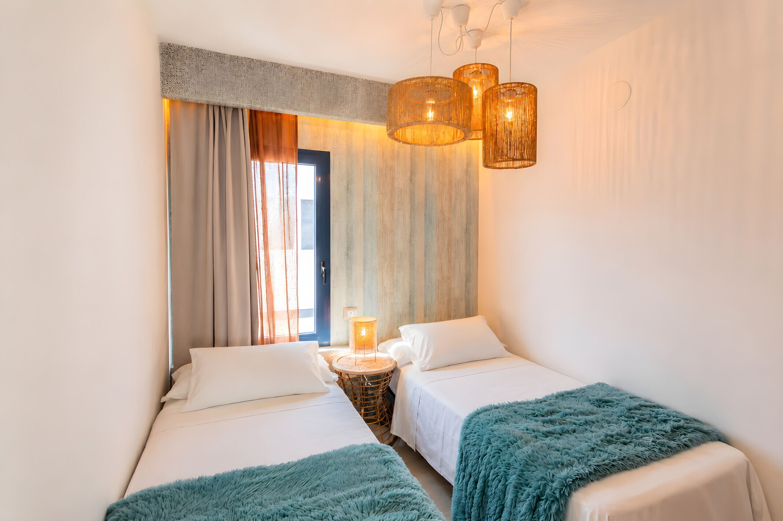 Ein Hotelzimmer mit zwei Betten, einem kleinen runden Tisch, einer Lampe und Blick ins Freie.