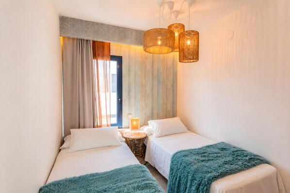 A hotel room with two beds, a small round table, a lamp, and a view of the outdoors. - Villa Arai (Playa Blanca)