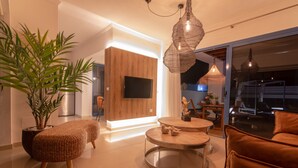 A modern living room with a large plant, wicker ottoman, round coffee table, and a sofa. - Villa Arai   (Playa Blanca)