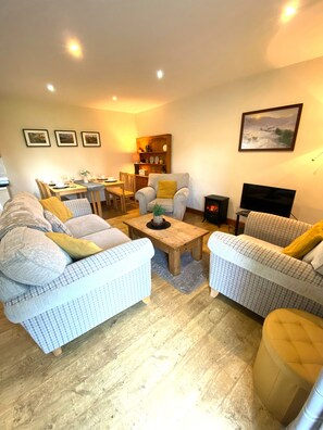 A cozy living room with two sofas, a coffee table, and a TV. There is a dining area with a table and chairs. - 5 Glantraeth Farm.  Pet friendly cottage, ideal base to explore Anglesey.... (Bodorgan)
