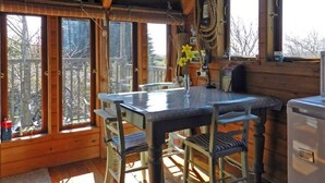 Interior de una cabaña de madera con cocina, ventanas amplias y vistas al exterior.