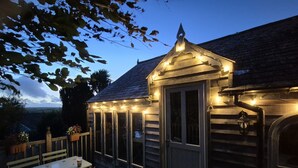 Una terraza de madera con zona de estar cubierta, una mesa y sillas.