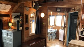 Interior de una cabaña con un banco de madera, una mesa de comedor con sillas, una kitchenette y un baño con ducha.