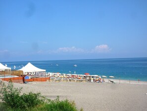 A beach with tents and umbrellas, a sandy shore, and the sea in the background.
