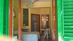 A bedroom with a bed, a desk, and a chair, a bathroom with a shower, and a dining area with a table and chairs. - Gardenhouse on the largest beaches of Taormina apartment n. 1 for 4 people (Mazzeo, Taormina)