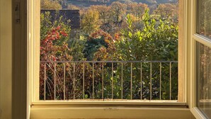 Ein Zimmer mit einem gro ßen Fenster, das einen Blick auf eine hügelige Landschaft mit Bäumen und einem Steinhaus bietet.