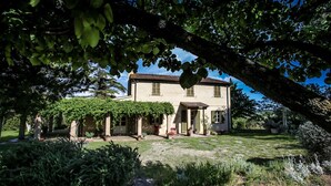 A two-story house with a garden in front, featuring a pergola covered with vines. - Charming Maremma Villa w/Swimming Pool, Countryside Serenity and Beaches Nearby (Magliano in Toscana)