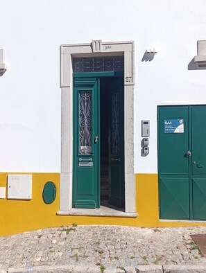 A green door with a decorative pattern, a mailbox, and a green utility box with a sign on a building with a yellow and white facade.