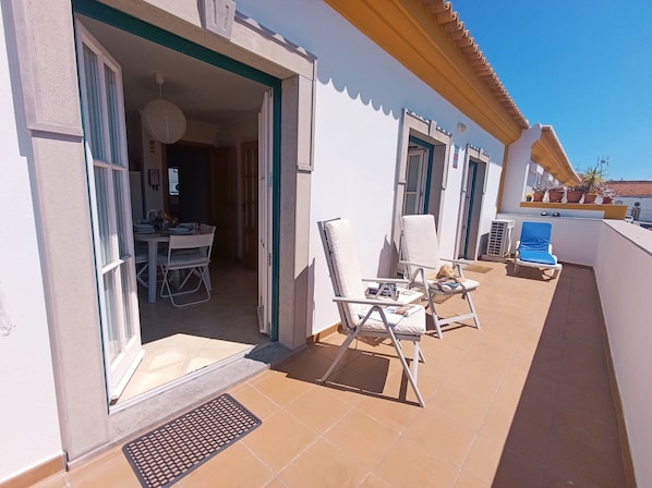 A balcony with outdoor seating, a dining area, and a door leading to an interior space.