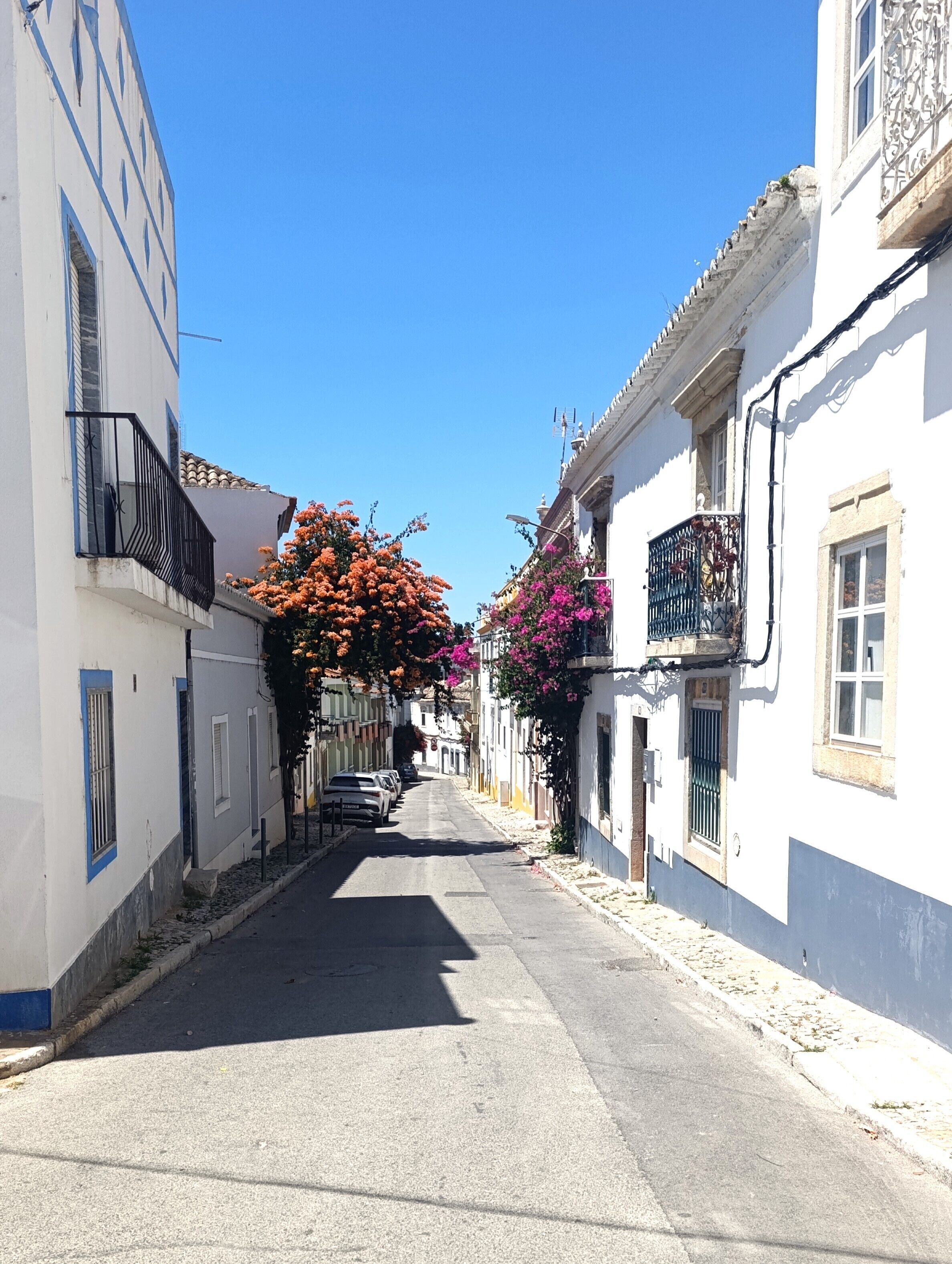 A narrow street lined with white buildings, some with balconies, and a clear blue sky.