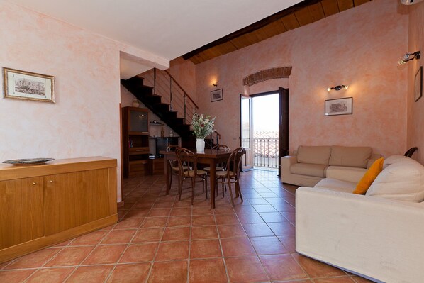 A spacious living area with a dining table, chairs, a sofa, a staircase, and a balcony.