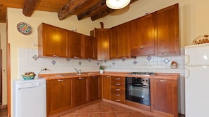 A kitchen with wooden cabinets, a white dishwasher, a stove, and a black oven. - Terrazza del Centro (Cefalù)