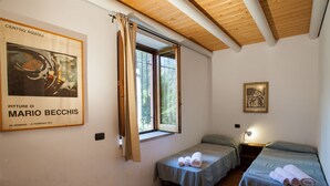 Een kamer met twee bedden, een raam met gordijnen, een kunstwerk in een lijst aan de muur, en een tafeltje met handdoeken.