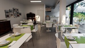 Een eetgedeelte met gedekte tafels, een keuken op de achtergrond, en een uitzicht op de natuur door grote ramen.