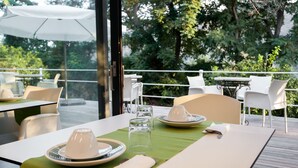Een terras met eettafels voor twee personen, met witte stoelen en een groene tafelkleed.
