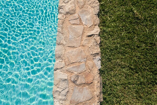 A stone pool edge with clear blue water and a grassy area beside it. - Sicily farmholidays:CASA DELLA PALMA,farmhouse with pool few minutes to the sea (Rocca di Capri Leone)