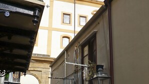 A narrow street with buildings on either side, a metal gate, and a small garden area with plants. - Wine House (Cefalù)