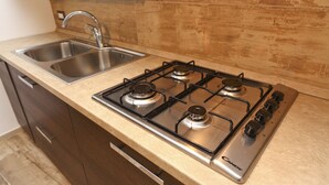 A kitchen with a stainless steel gas stove, a double sink, and wooden cabinets. - Wine House (Cefalù)