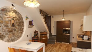 A cozy interior with a stone wall, a dining area with orange chairs, a staircase, and a kitchen with modern appliances. - Wine House (Cefalù)