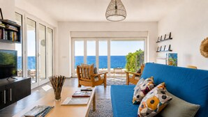 A modern living room with a blue sofa, a wooden coffee table, and a view of the sea through large windows. - 10 meters from the beach – Marina Holiday Home, oceanfront in Pizzo, Calabria (Pizzo)
