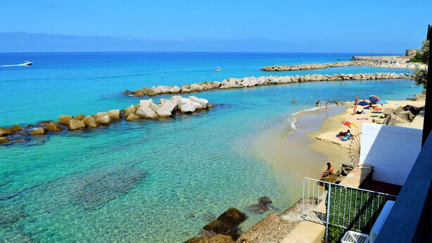A beach with clear turquoise water, rocky breakwaters, and a few people enjoying the sun. - 10 meters from the beach – Marina Holiday Home, oceanfront in Pizzo, Calabria (Pizzo)