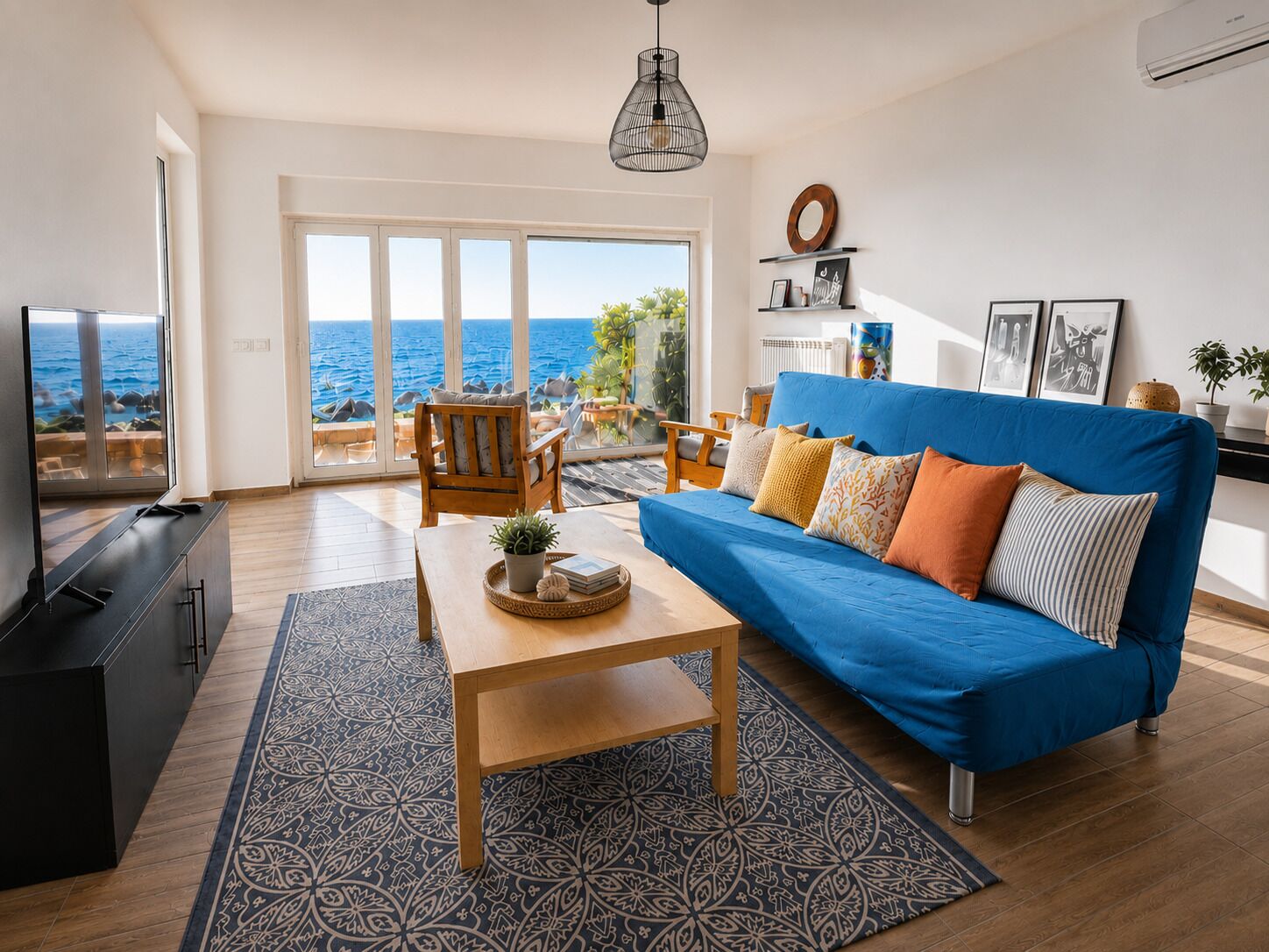 Ein Wohnzimmer mit blauem Sofa, einem Holztisch und Meerblick durch große Fenster.