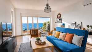A living room with a blue sofa, wooden coffee table, and a view of the sea through large windows. - 10 meters from the beach – Marina Holiday Home, oceanfront in Pizzo, Calabria (Pizzo)