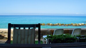 A seaside view with a stone wall, a wooden chair, and a table with a potted plant. - 10 meters from the beach – Marina Holiday Home, oceanfront in Pizzo, Calabria (Pizzo)