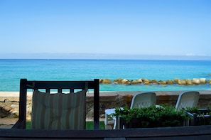 Blick auf das Meer mit einer Steinmauer, einem Holzstuhl und einem Tisch mit einem Blumentopf.