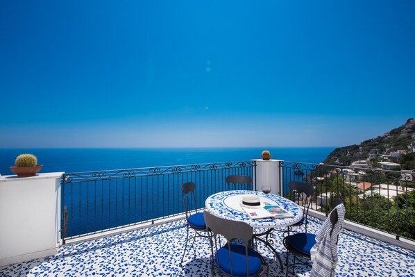 A terrace with a view of the sea, a round table with chairs, and a cactus plant.