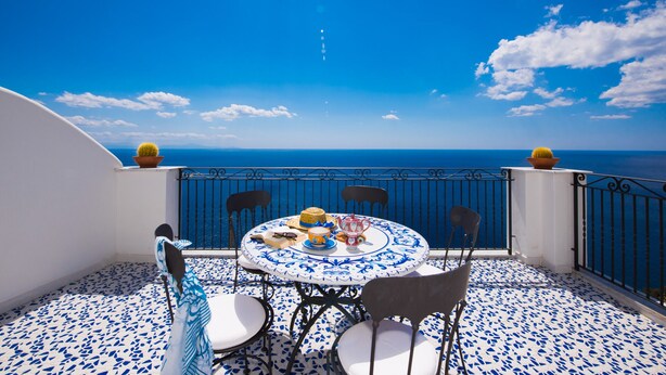 Une table ronde entourée de chaises, sur un balcon offrant une vue sur la mer.
