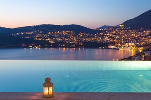 Una piscina con un farol en el borde, rodeada por un paisaje urbano al anochecer.
