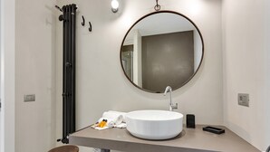 Une salle de bain moderne avec un miroir rond, un lavabo blanc et un porte-serviettes.