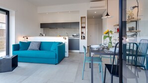 Un espace de vie moderne avec un canapé de couleur turquoise, une table à manger avec des chaises et un coin cuisine doté de meubles gris.