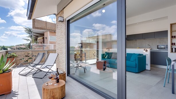 Un appartement moderne doté d’une porte vitrée donnant sur un balcon, d’une cuisine et d’un espace de vie avec un canapé bleu.