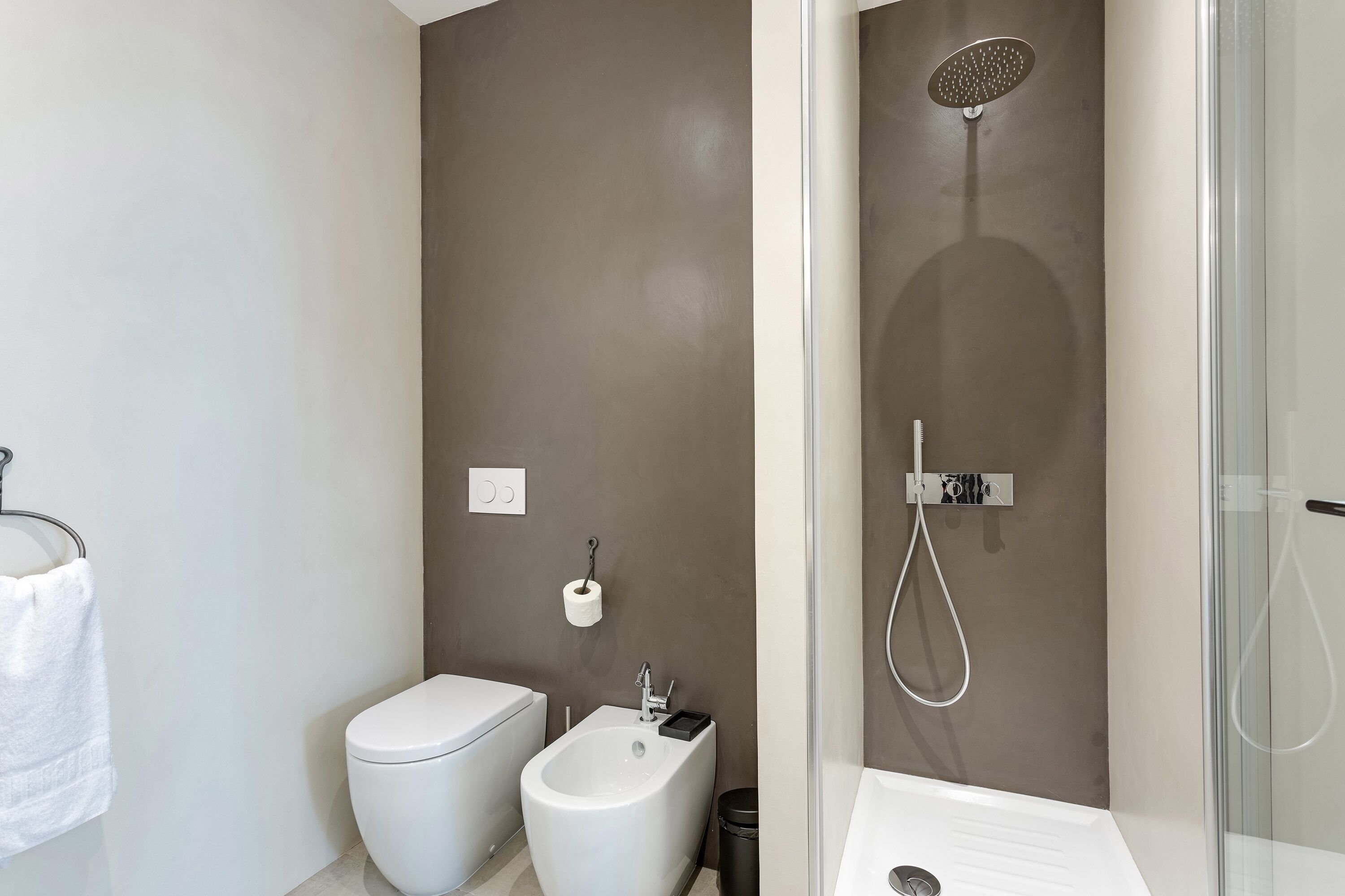 Une salle de bain moderne équipée de toilettes, d’un bidet et d’une douche séparée par des parois en verre.