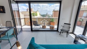 Une chambre moderne avec un grand lit, un bureau avec une chaise, une petite table avec une lampe, et une vue sur la ville grâce à de grandes fenêtres.
