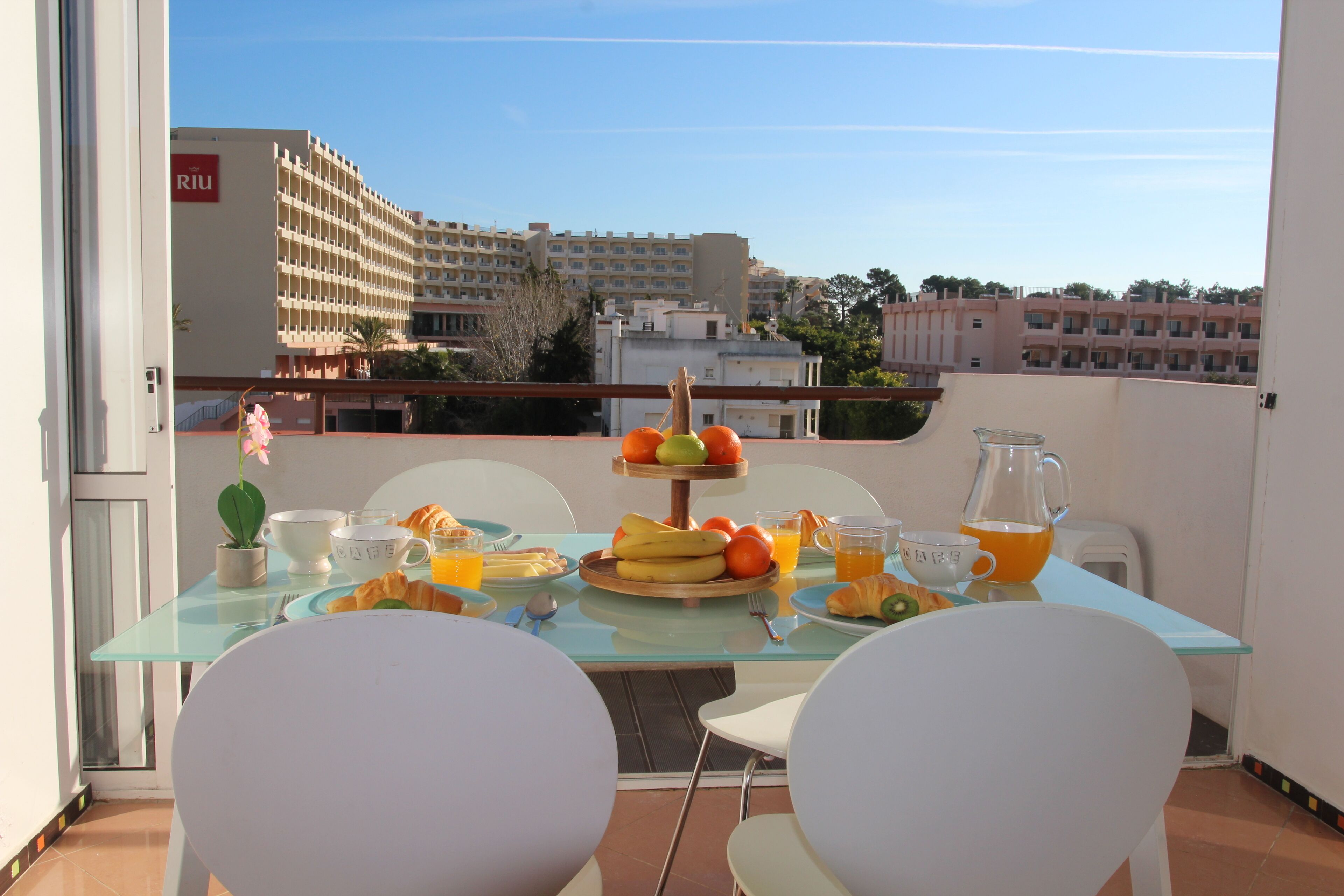Een balkon met een ontbijttafel, compleet met croissants, fruit en drankjes.