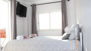 A bedroom with a bed, a TV mounted on the wall, a window with curtains, and a bedside table with a lamp. - At 300 m from the beach, a 2 bedroom penthouse with an amazing terrace.  Center, cable tv (Albufeira)