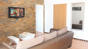 A living room with a stone wall, a flat-screen TV, a white coffee table, a brown leather sofa, and a door with a mirror. - At 300 m from the beach, a 2 bedroom penthouse with an amazing terrace.  Center, cable tv (Albufeira)