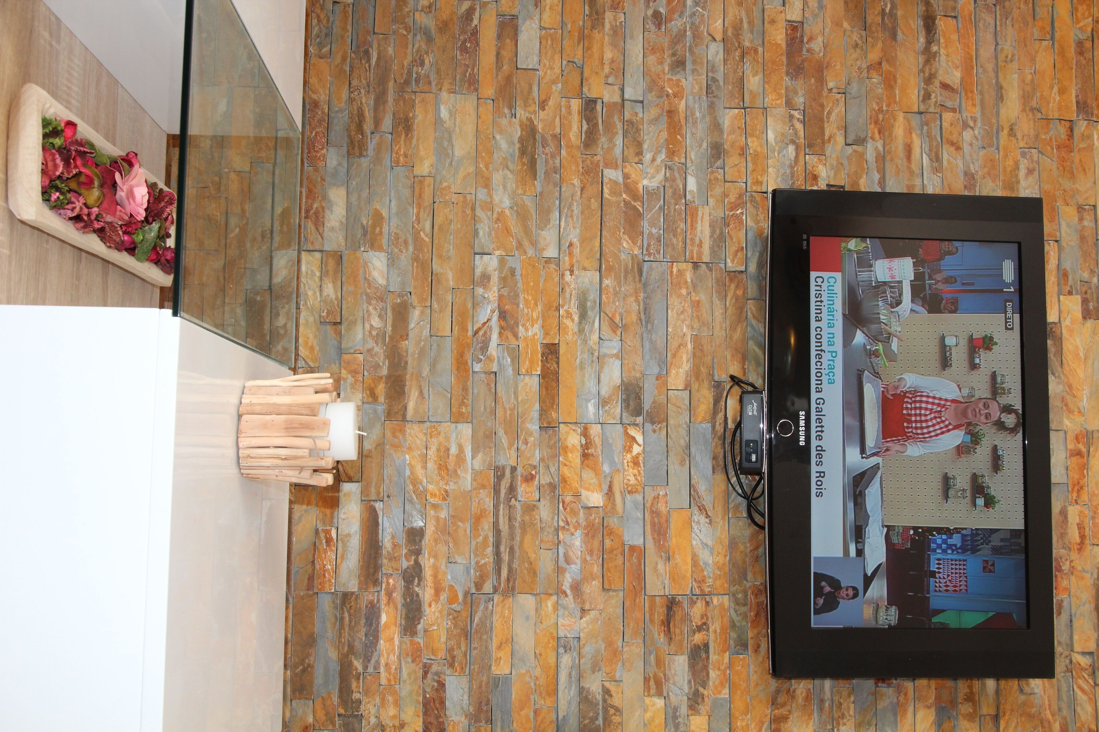 A wall with a patterned tile design and a framed television displaying a cooking show.