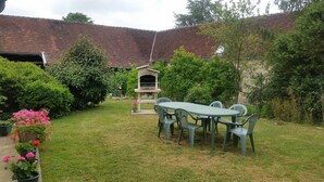 Un jardin avec un barbecue, une table et des chaises, ainsi que des plantes en pot.
