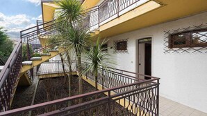 A multi-story building with a yellow facade, a staircase with metal railings, and a small palm tree in the courtyard. - Residence -2 Saint Benedict of Lugana (Peschiera Del Garda)