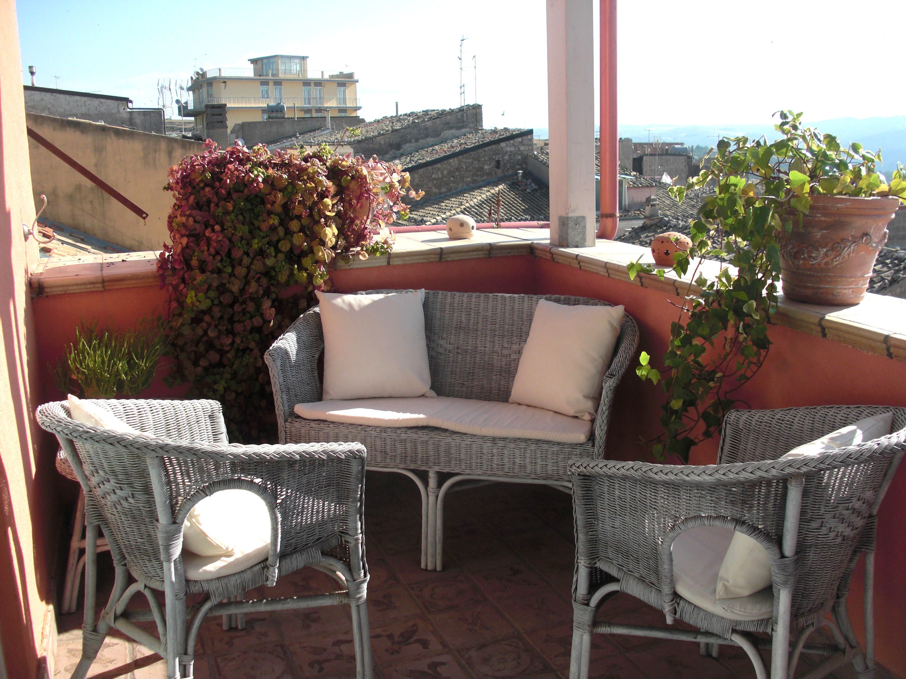 A balcony with wicker furniture, a potted plant, and a view of the cityscape.