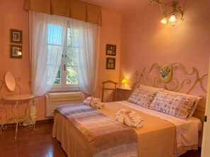 A bedroom with a bed, a bedside table, a window with curtains, and wall-mounted lights.