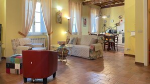 Un salón acogedor con techo de madera, un sillón rojo, un sofá estampado y una zona de comedor con mesa y sillas.