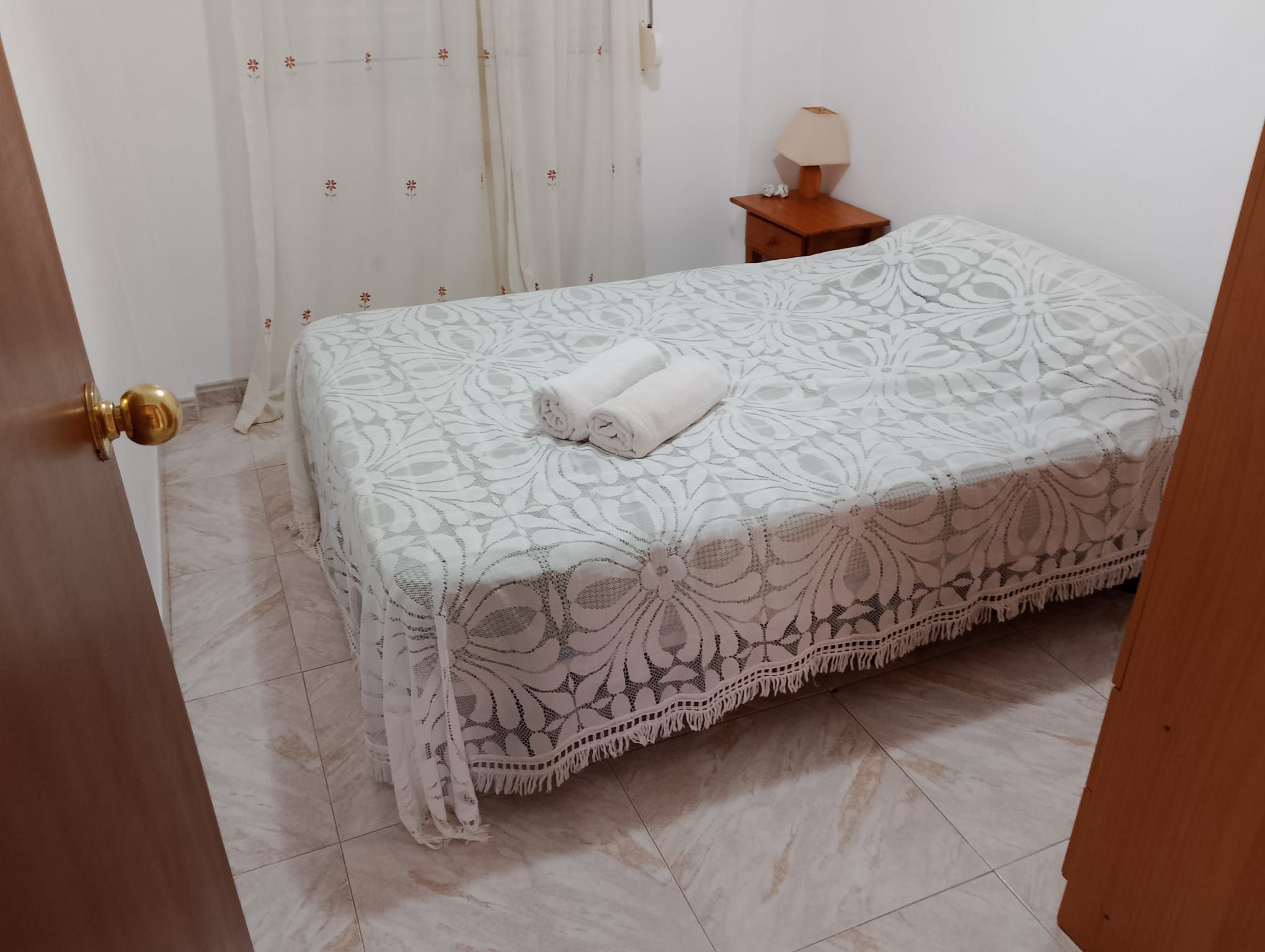 A bedroom with a bed, a nightstand, a lamp, and a door.