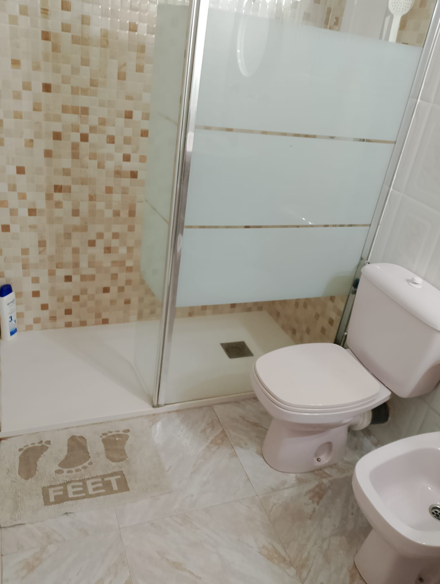 Un baño con inodoro, bidé y una cabina de ducha de vidrio.