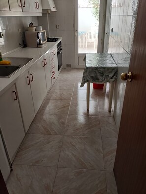 A kitchen with white cabinets, a sink, and a table with a leaf-patterned tablecloth. - Apartment Club Nautico (Los Nietos)