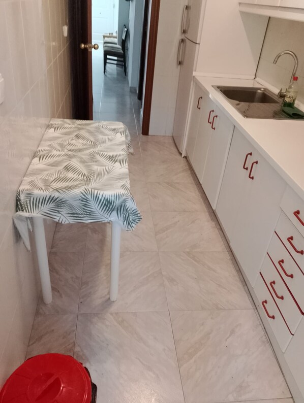 A small kitchen with a white table, a red trash bin, and cabinets with red handles.
